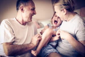Grandmother and grandfather with hearing loss play with their granddaughter and after getting a hearing aid at an affordable price can hear their granddaughter laugh again..