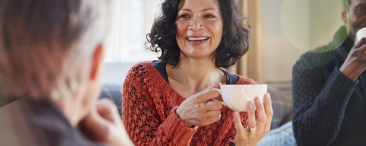 Middle aged woman meeting friends around table, wearing her best online hearing aid.
