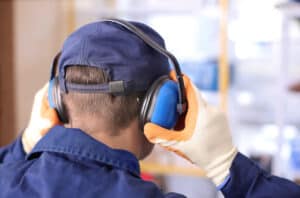 Man wearing hearing protectors to protect his ears in the workplace to prevent possibly having to see a hearing aid specialist due to a hearing loss.