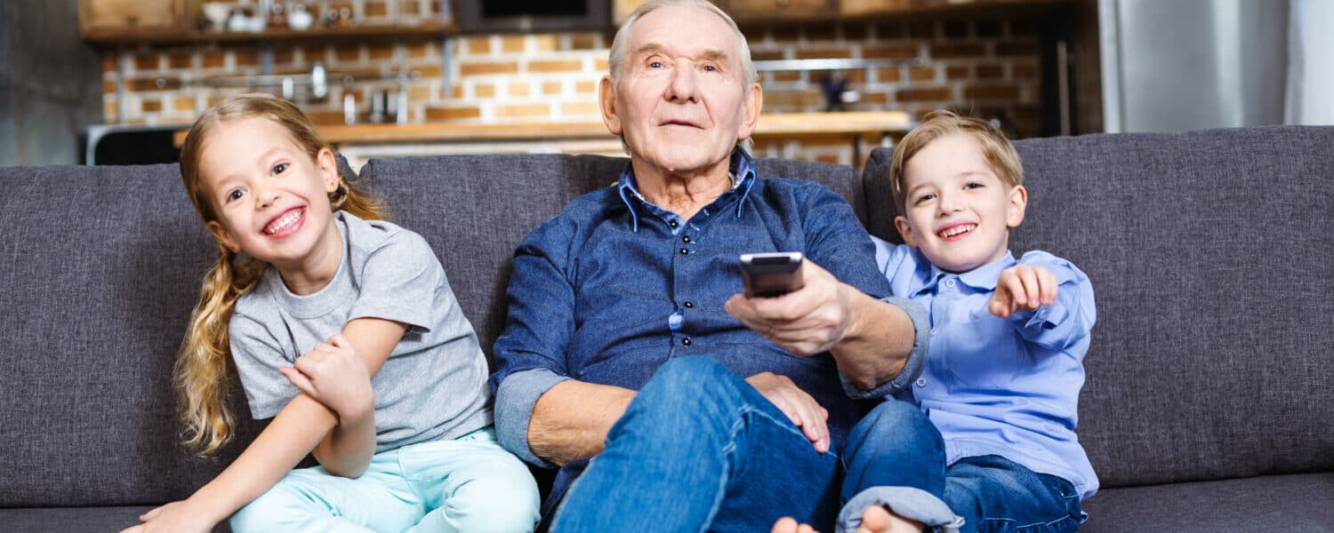 Man wearing best value hearing aids (Lexie Lumen hearing aids) with a hearing aid companion microphone watches television with grandchildren