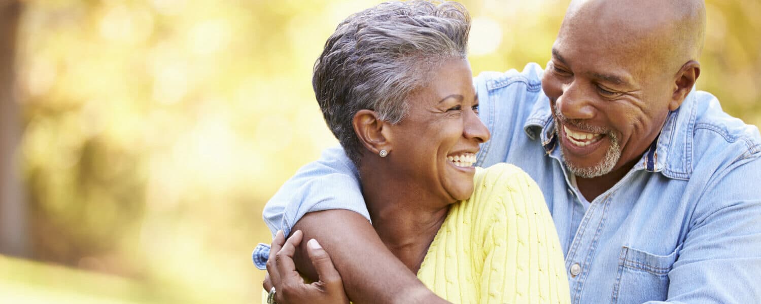 Senior couple embracing and smiling, man wears the best hearing aid available on the Lexie hearing website.