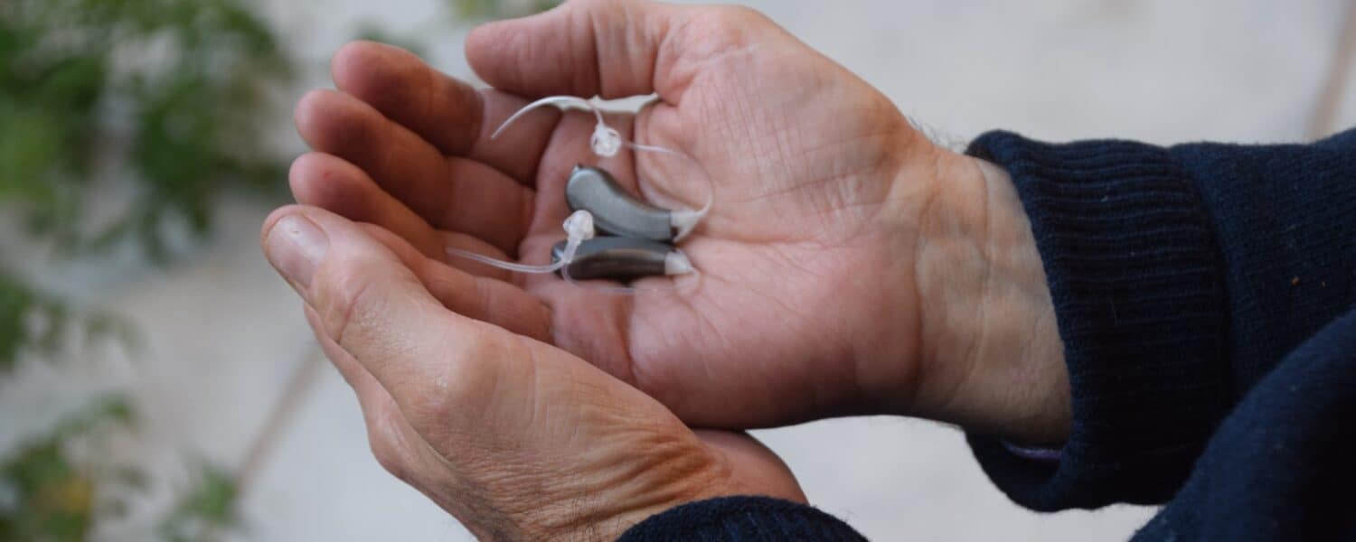 Very small and invisible Lexie Lumen hearing aids in palm of man's hands.