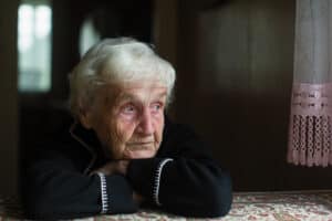 Depressed older woman looks out of the window sadly as she is in serious need of a premium hearing aid