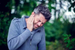 Middle-aged man with tinnitus standing in a garden. He is in pain and considering getting a hearing aid at an affordable price to help with his tinnitus symptoms