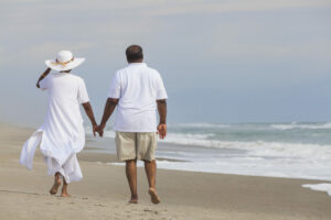 African American couple walking along the seashore holding hands and discussing wearing Lexie Lumen hearing aids in windy conditions