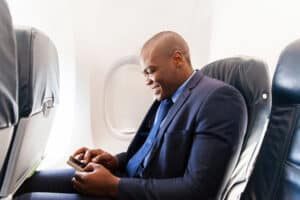 Man sitting on on airplane with his smartphone in his hand wearing invisible hearing aids to asssisting him with traveling with a hearing loss