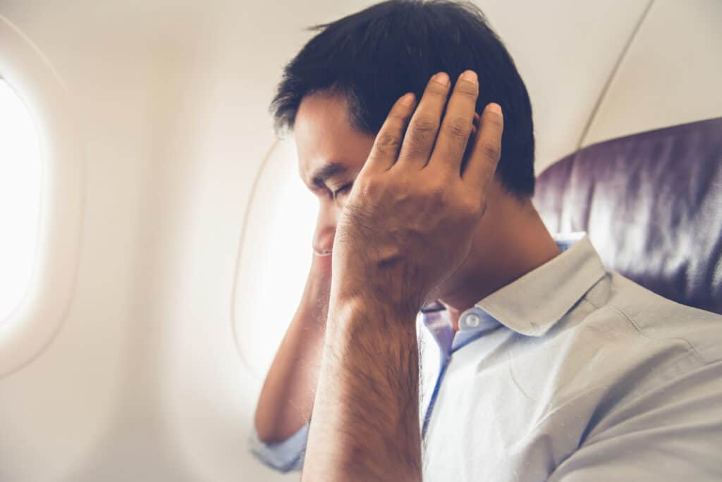 Man sitting on an airplane with his hands over his ears