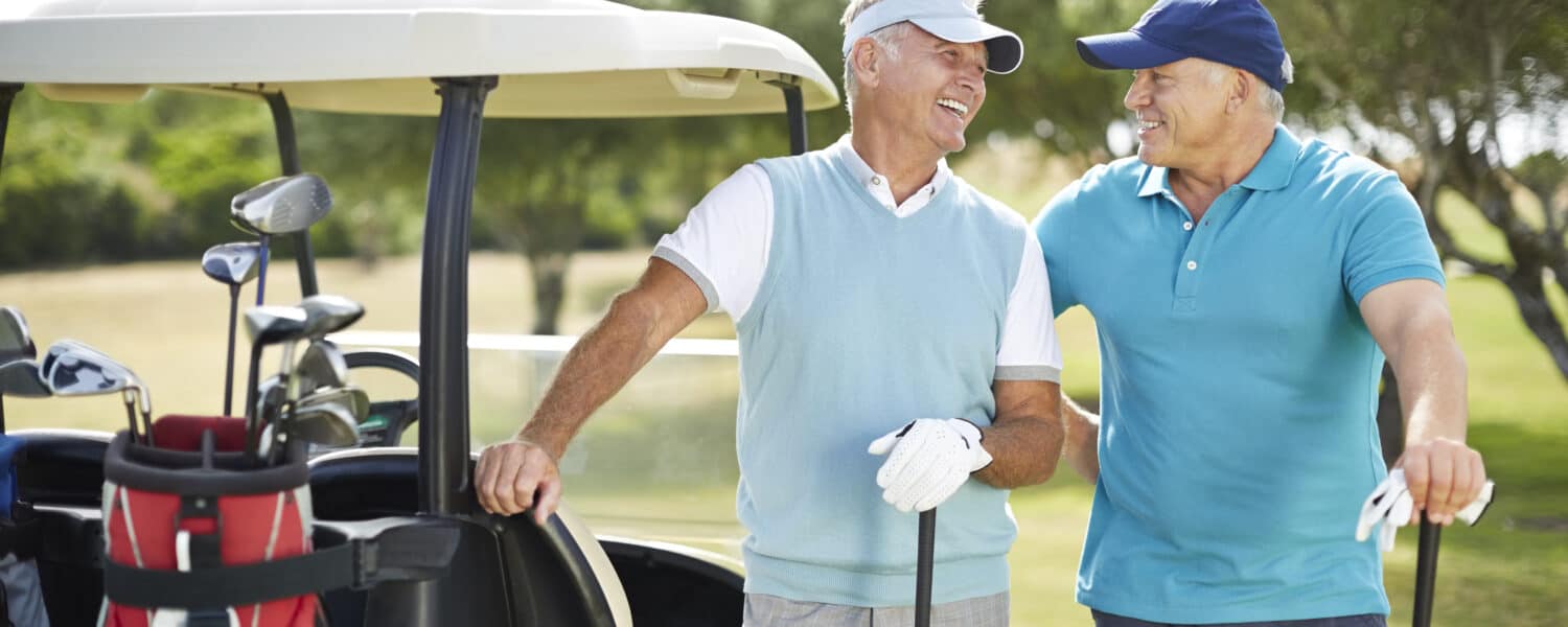 Two men wearing premium hearing aids outside while playing golf