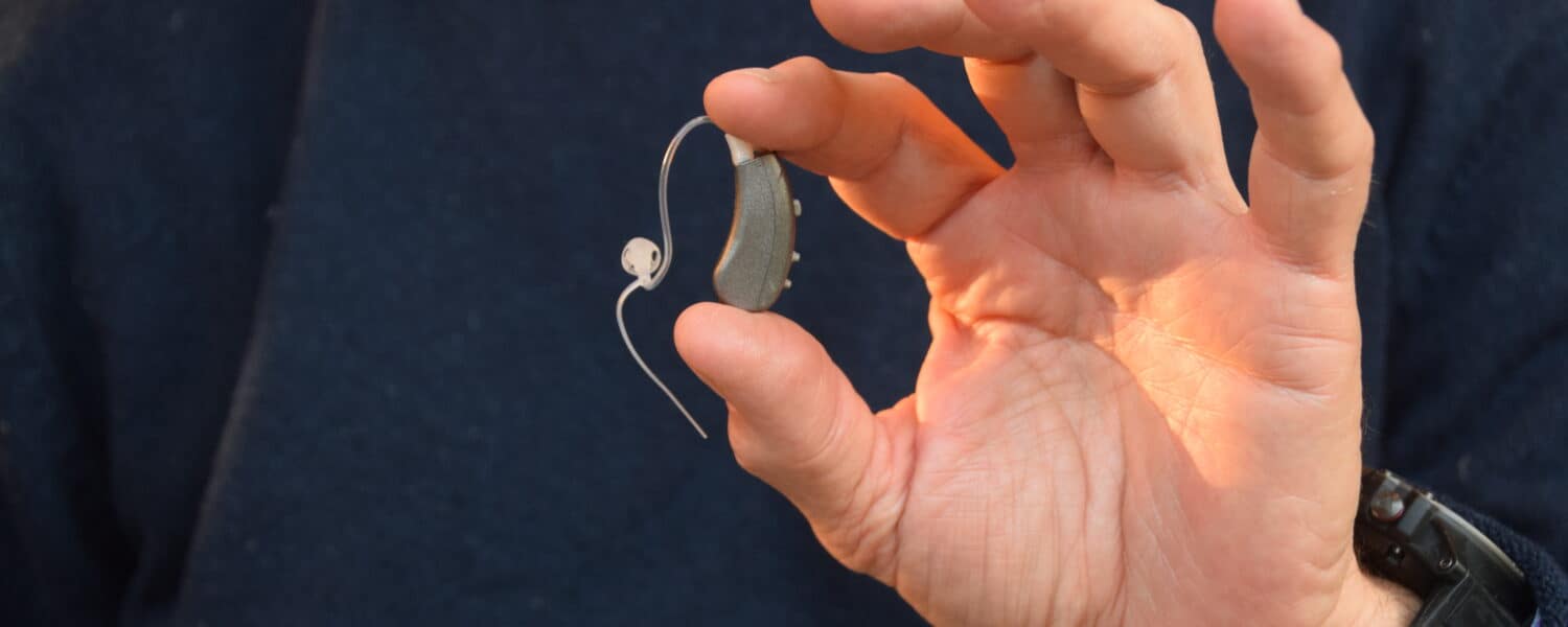 Man holding the Lexie hearing aid in in hand, thinking about hearing aid prices.