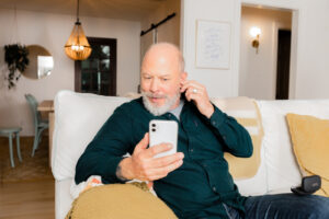 Man sitting on the couch talking with a hearing expert over the phone about hearing aid care.
