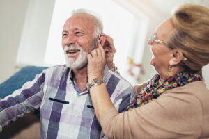 communicating with people who have a hearing loss Woman inserting over the counter hearing aids into a man's ear in their home.