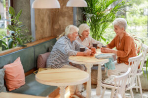Three elderly woman sitting in a cafe having coffee while using their hearing sense to communicate with each other