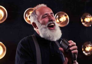 Elderly man siging into a microphone, he is singing with hearing aids