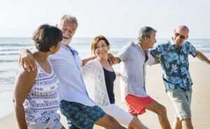 Group of older frienda embraxing each other on the beach, happy that hearing aids are fashionable