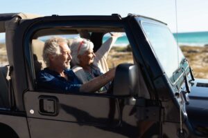 Man and woman driving in a car along the beach while listening to loud music