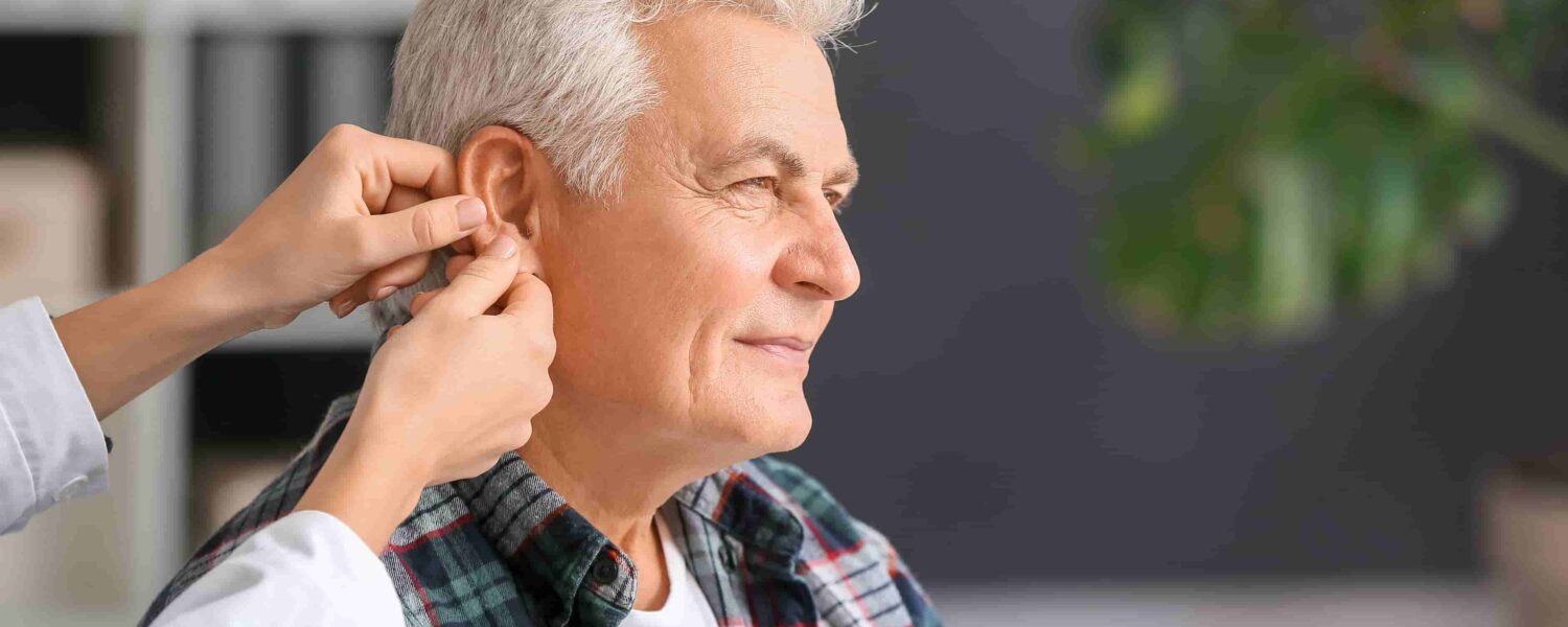 Woman inserting a hearing aid into a man's ear talkin of how to prevent hearing aids from falling out