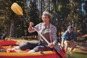 Woman on a kayak rowing on a river wearing waterproof hearing aids.