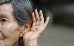 A senior woman with temporary hearing loss cupping her ear to hear better