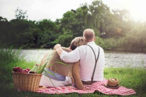 Senior man and woman sitting next to a lake having a picnic
